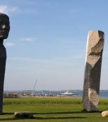 Zwei der Steinstatuen von Dodekalitten mit dem Fährhafen von Kragenäs im Hintergrund