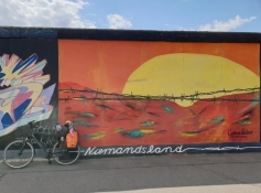 Min cykle foran et vægmaleri, som forestiller en solnedgang bag pigtråd